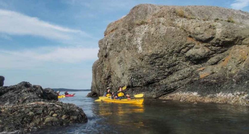 two people in a yellow kayak paddle between two rock formations on an outward bound course